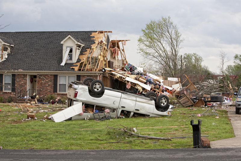 A home damaged by a tornado and an upside down truck in a yard.
