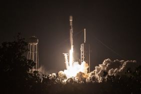 Fire and smoke is seen below a launching SpaceX rocket, with a dark sky in the background.