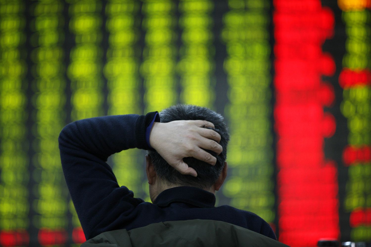 BAck view of an investor holding his head while looking at a ticker board.