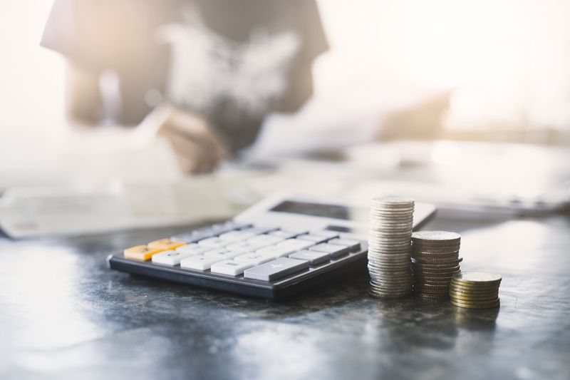 A close-up of calculator and coins with a person analyzing financial data.