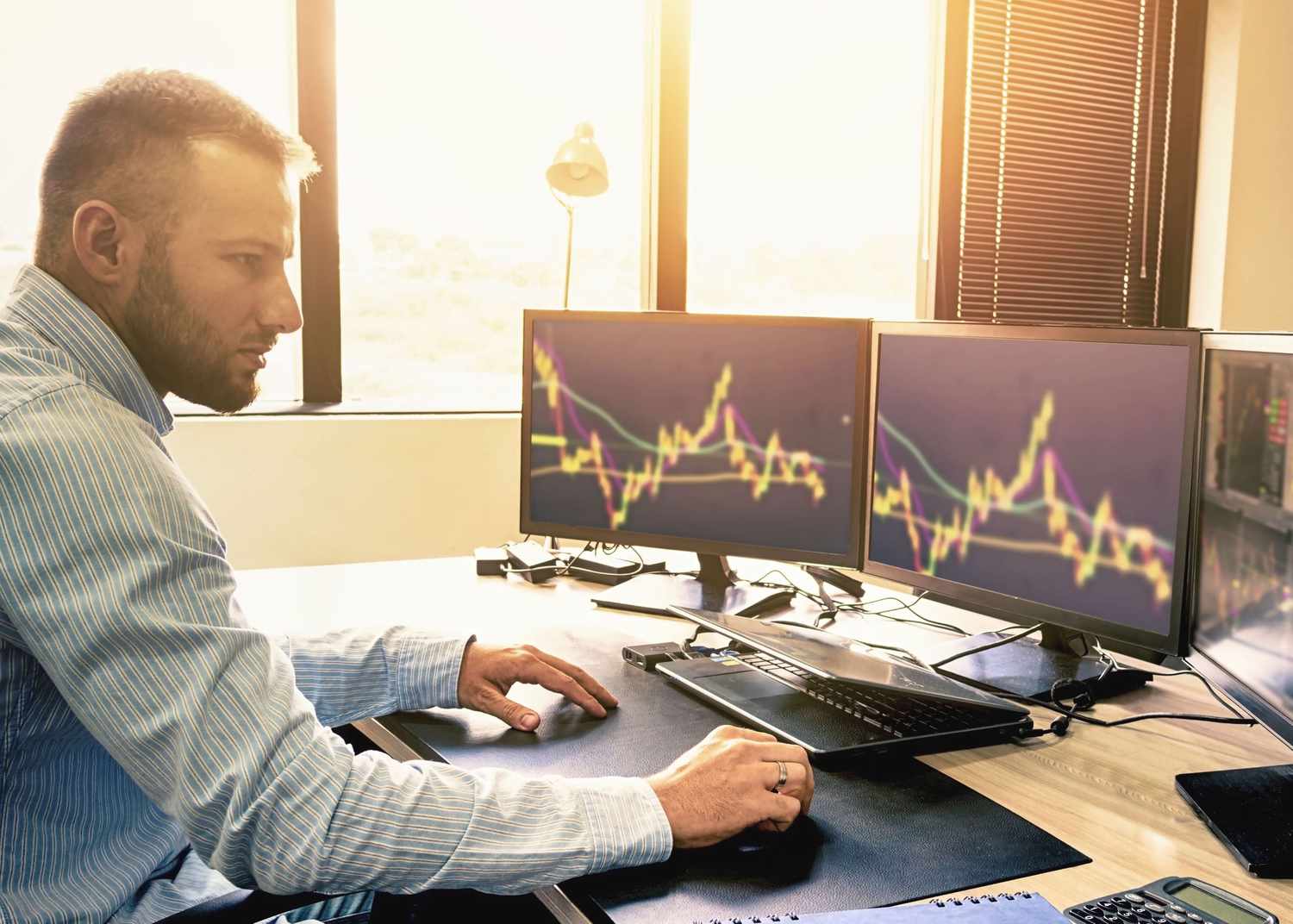 A day trader at his desk watching the market on his computer screens
