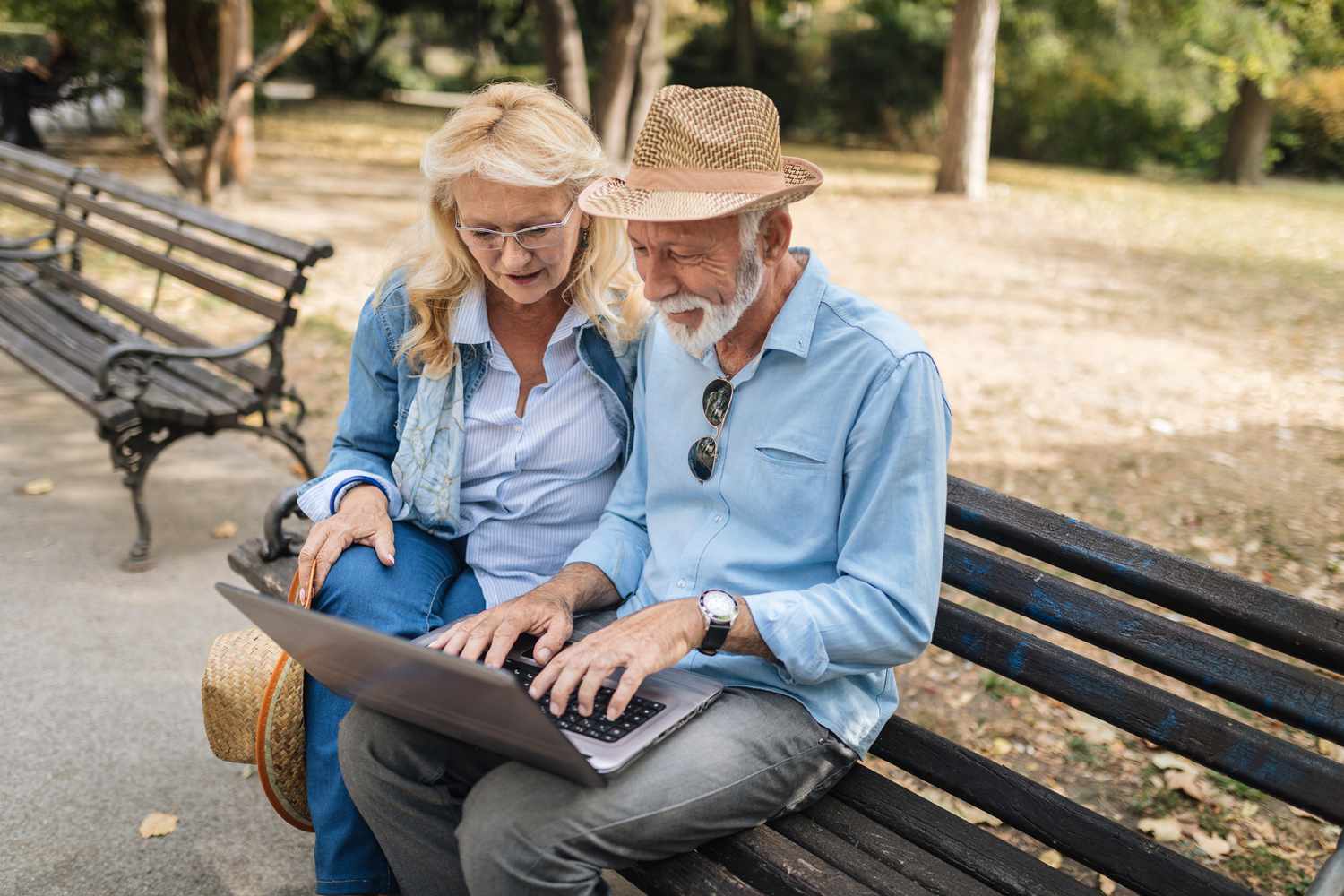 Two annuitants sit on a park bench and use a laptop computer and check the balance of their whole life annuity account.