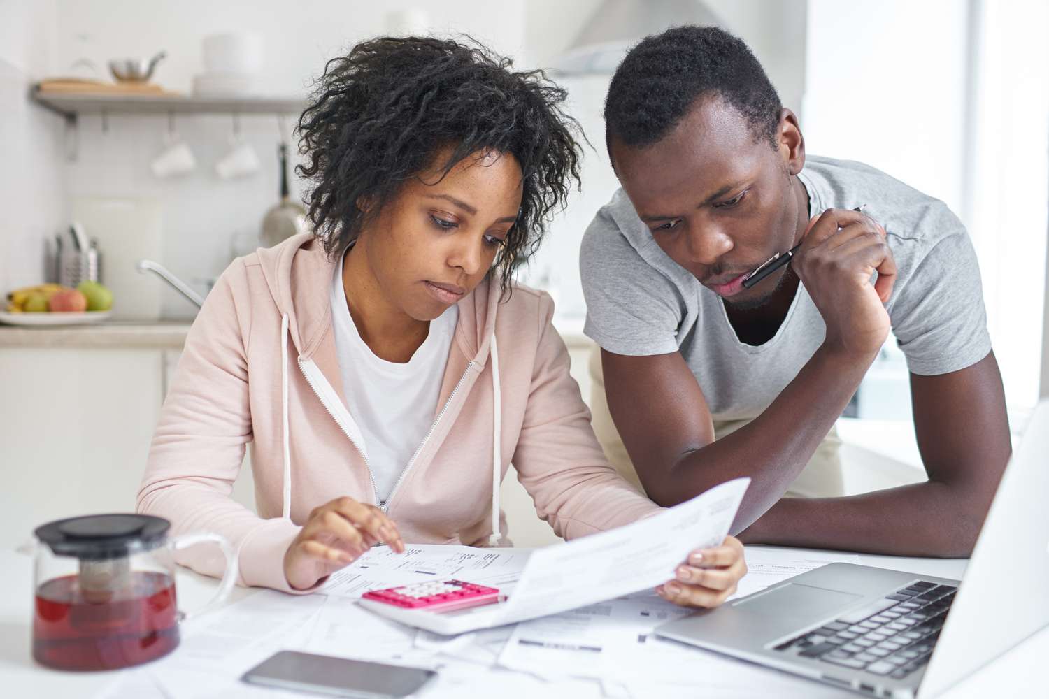 Young couple in their kitchen, looking with concern at mortgage documents and online rates