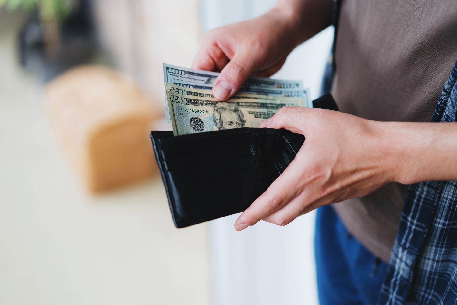 A person taking U.S. dollars in various denominations out of a wallet.