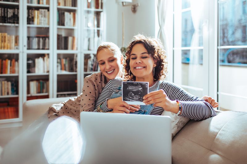 Expectant parents on couch show sonogram during video chat