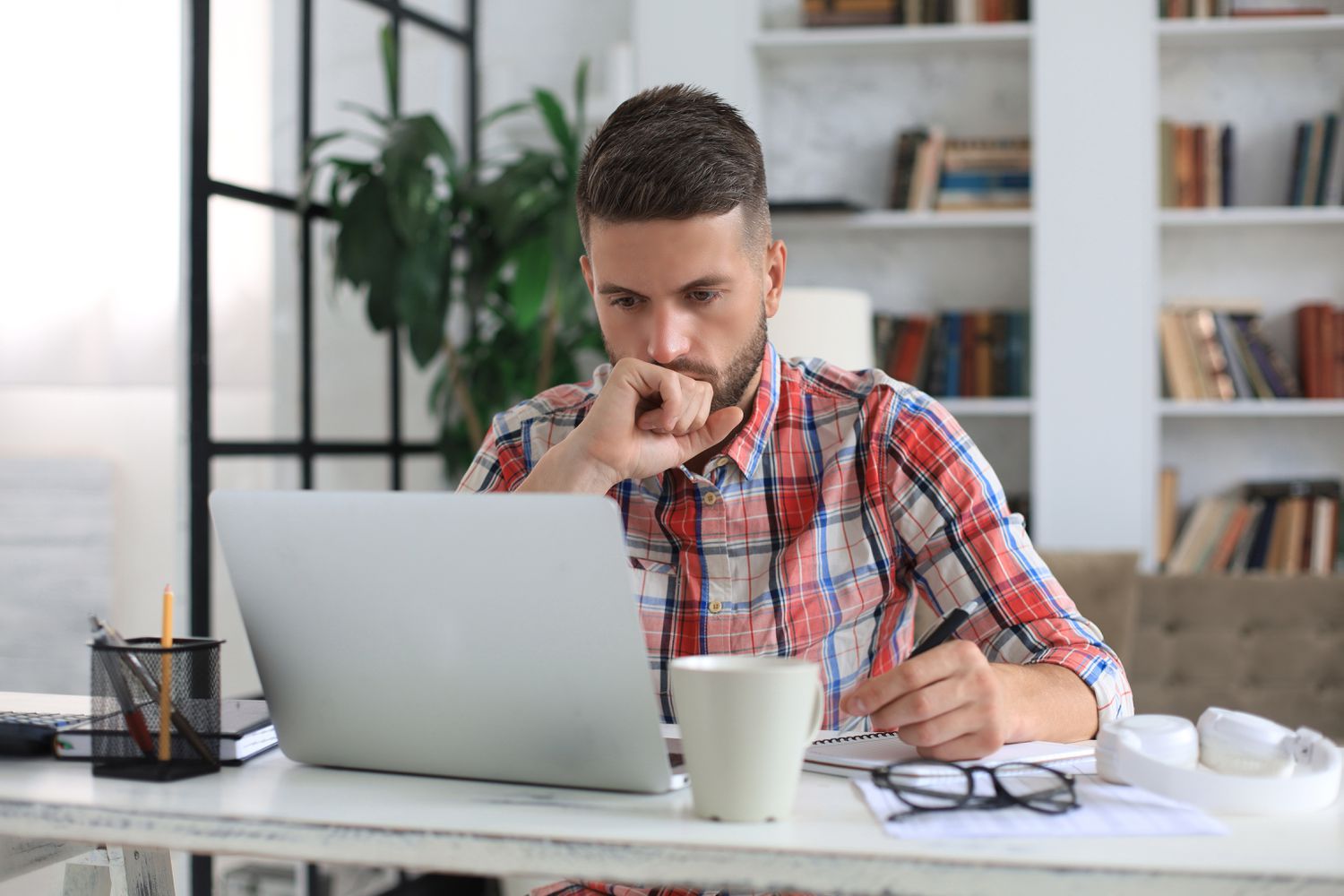 Young man sitting at a desk at home and looking intently at his laptop.