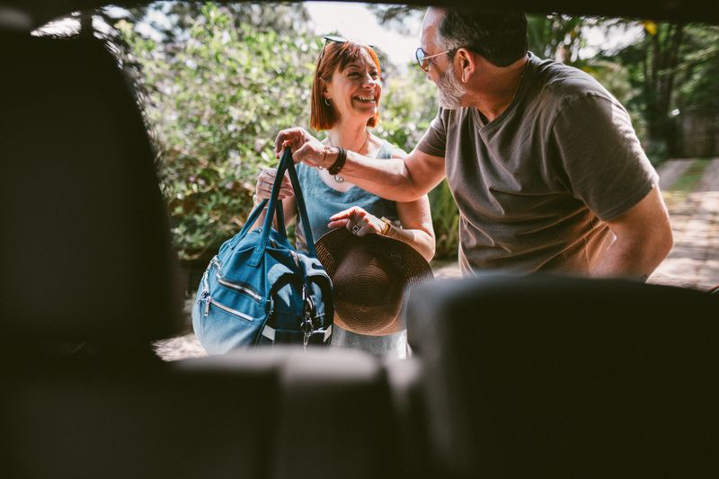 Smiling mature couple packing their luggage into the trunk of their car while leaving for a weekend getaway.