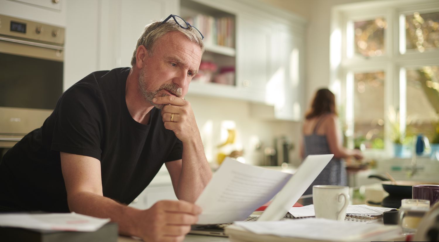 A middle-aged man sorts bills in his kitchen. 