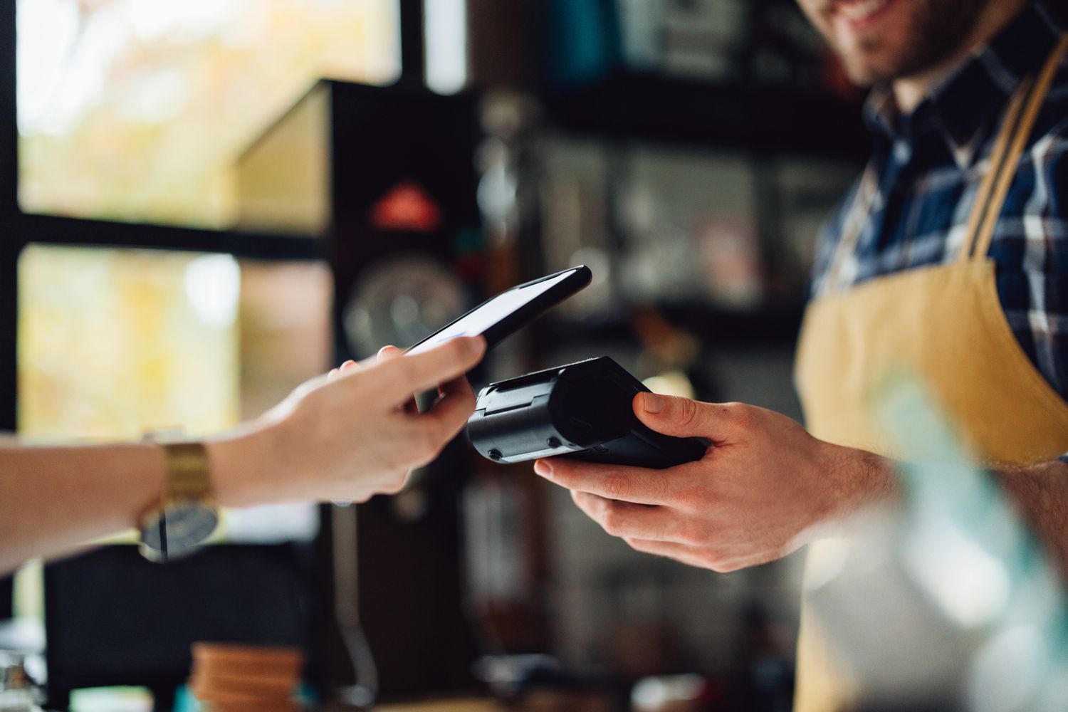Anonymous man is holding a card machine while the other person is placing their phone to pay