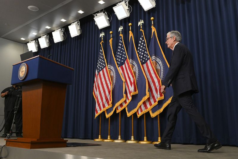 Jerome Powell walks across a stage, toward a podium. Behind him are U.S. and Federal Reserve flags.