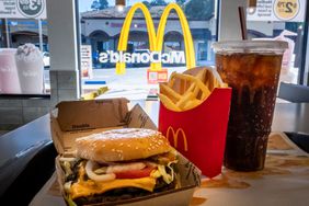 A double quarter pounder with cheese, French fries, and a large drink sit on a table in front of a window with the McDonald's logo.