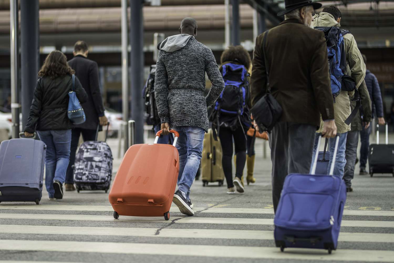 Travelers walking toward an airport terminal while pulling suitcases