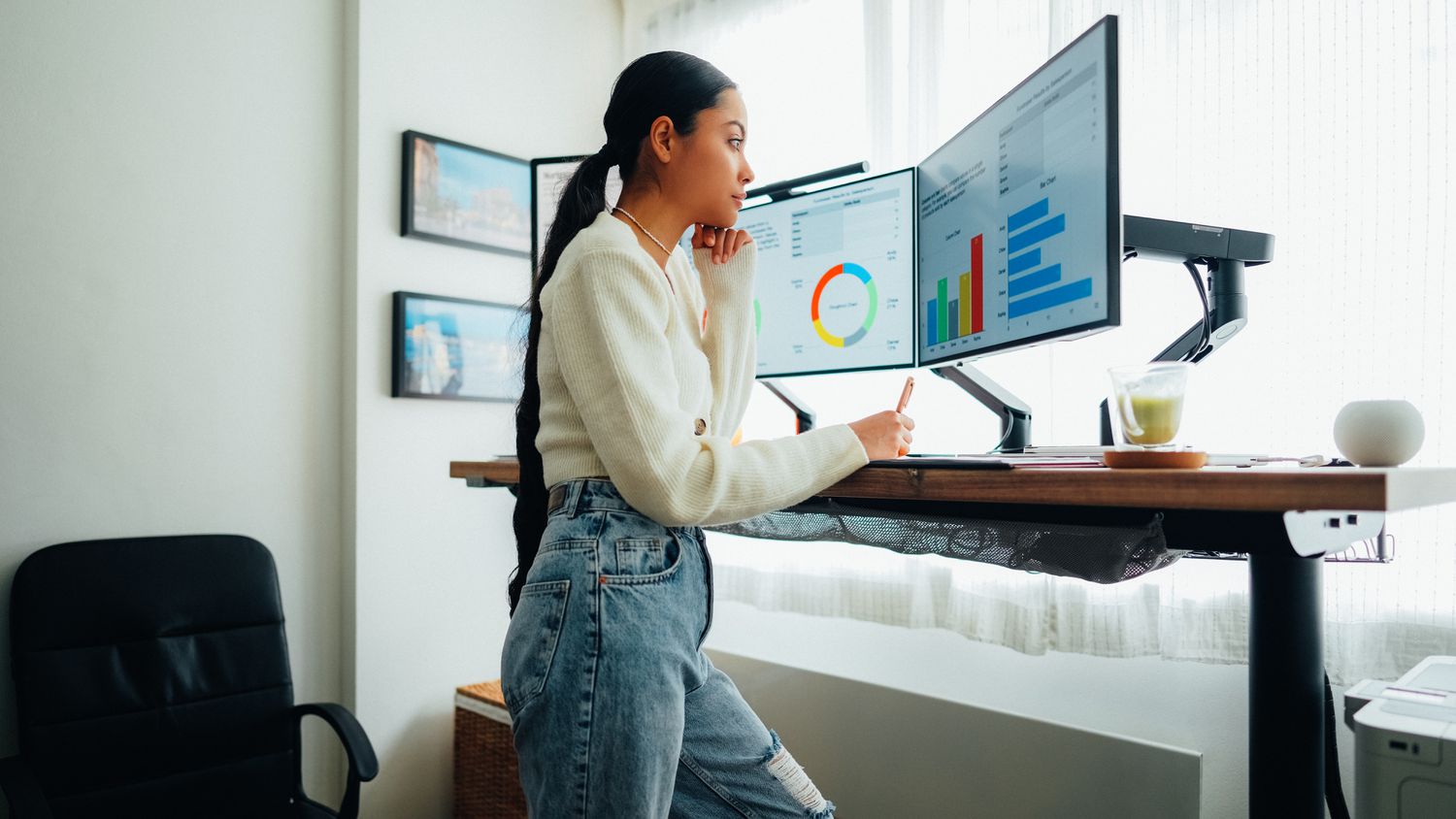 Woman working on a computer at a standing desk. The screens display colorful charts. 