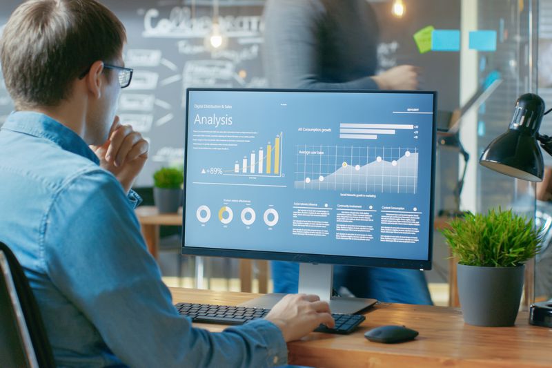 An analyst works on a personal computer showing statistics.
