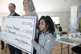 Girl helping hold large donation check in community center