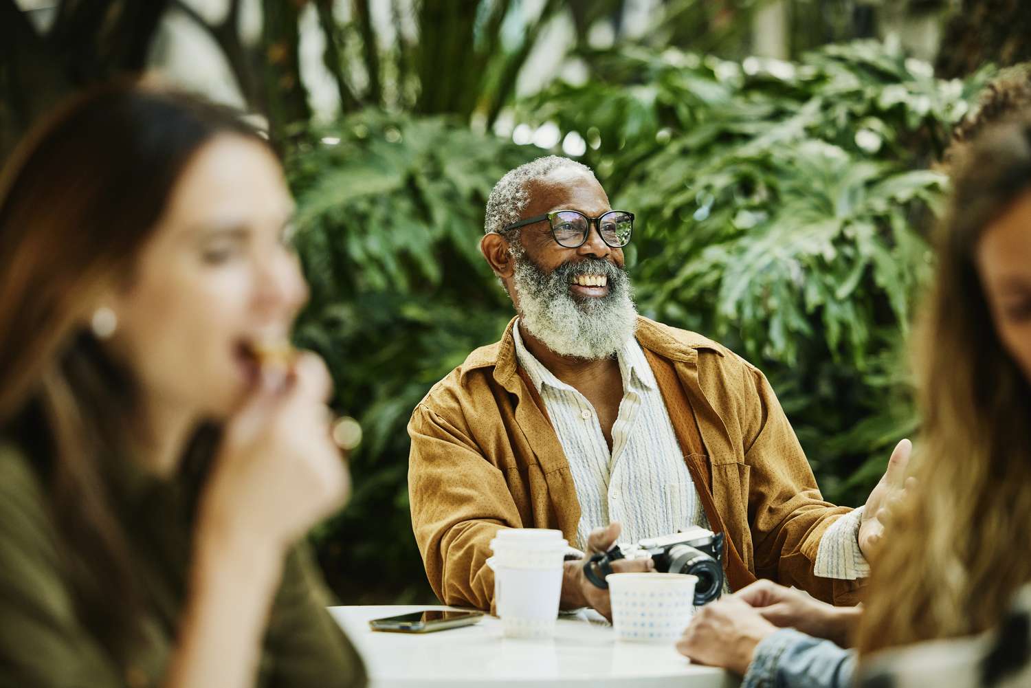 Smiling man with gray hair and a beard sitting in an outdoor cafe holding a camera.