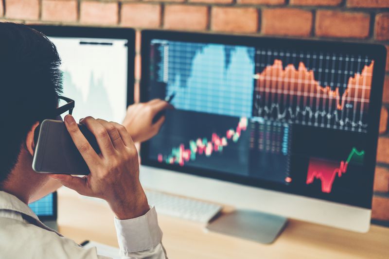 Stock broker on the phone looking at a computer screen with financial information