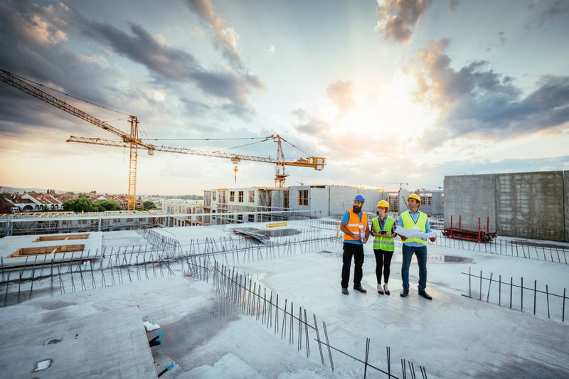 Three people wearing protective equipment look over a construction site
