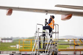 An employee prepares to attach a refueling hose to a passenger aircraft.
