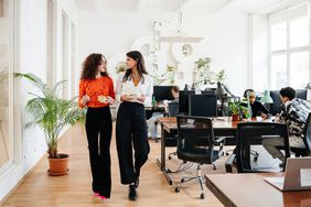 Two female business colleagues walking and talking in a modern office