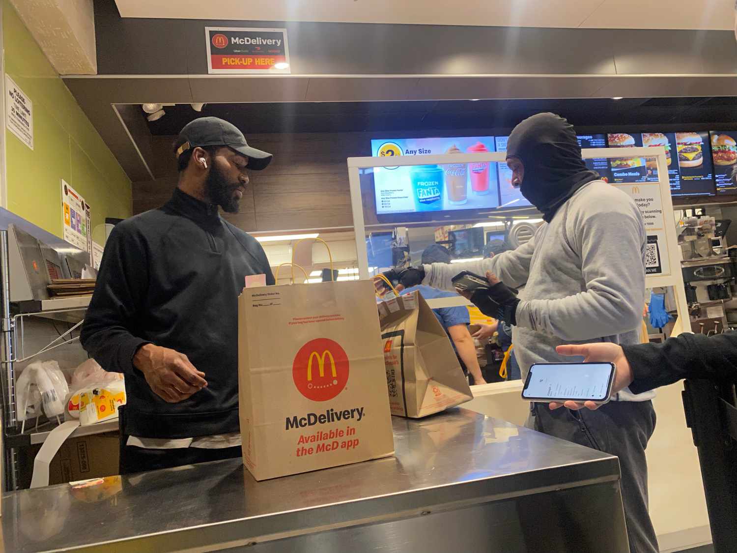 Delivery Person showing order on smart phone to employee at McDonalds pick up, Queens, New York. 