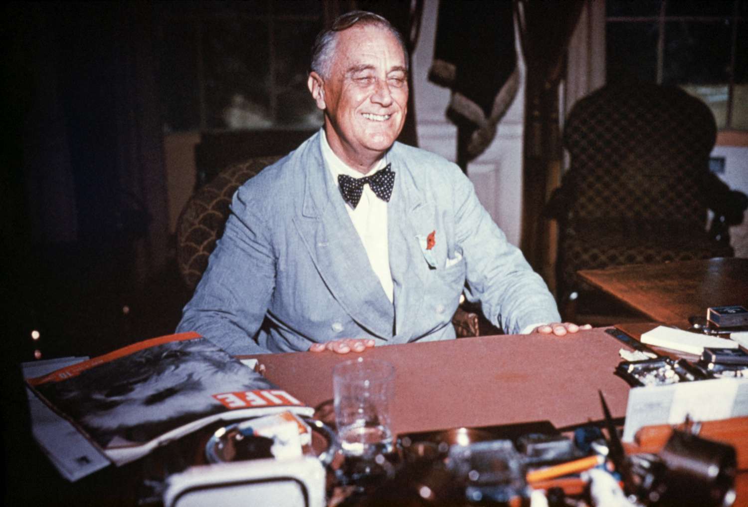 Portrait of Franklin Delano Roosevelt seated at his desk, smiling. Undated color slide.