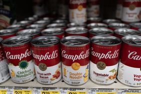 Rows of red and white Campbell's soup cans are seen on a shelf in a grocery store.
