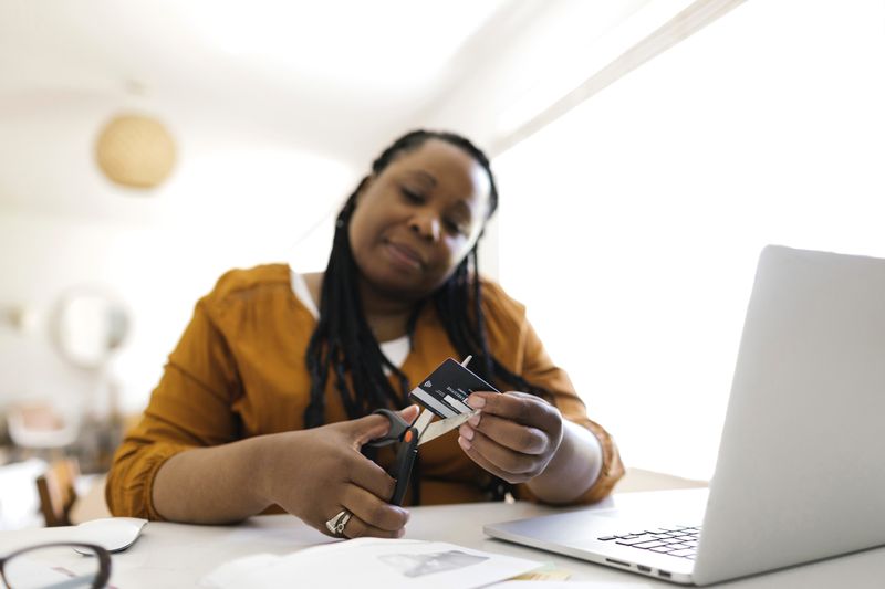 Some cutting up their credit card with scissors while seated with a laptop.