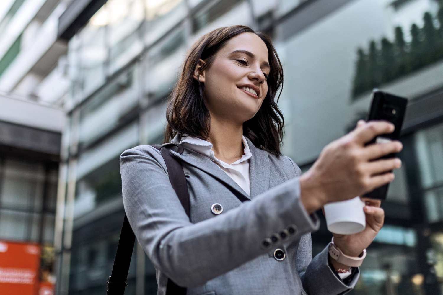 Woman drinking coffee and using mobile phone in front of the office