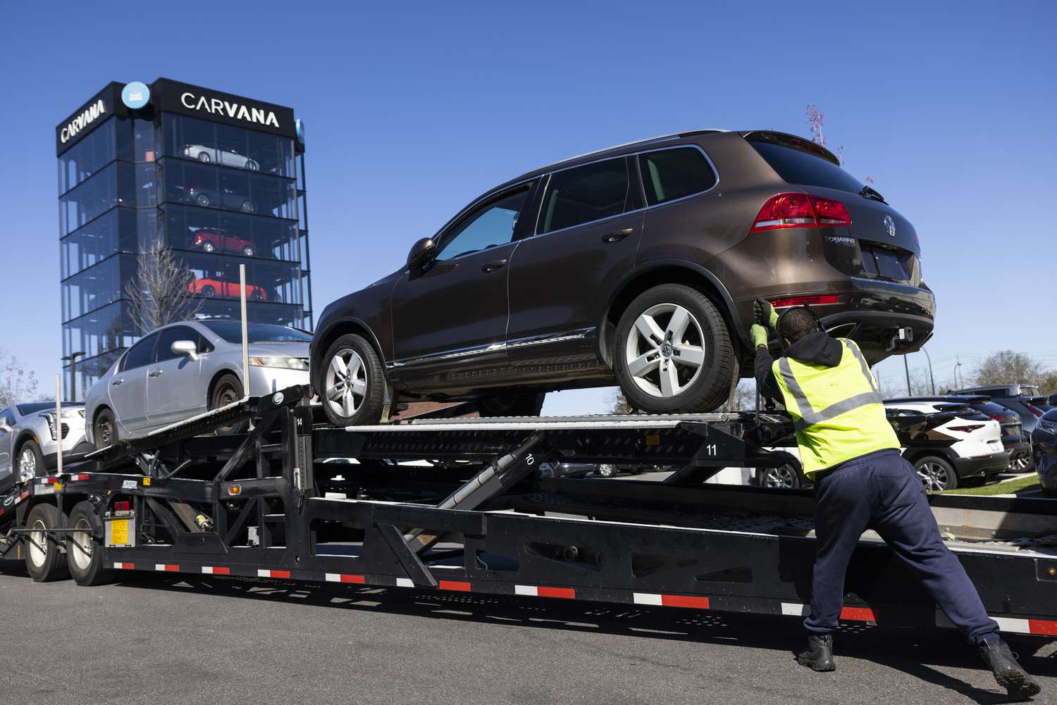A worker loads vehicles onto a transporter near a Carvana location 