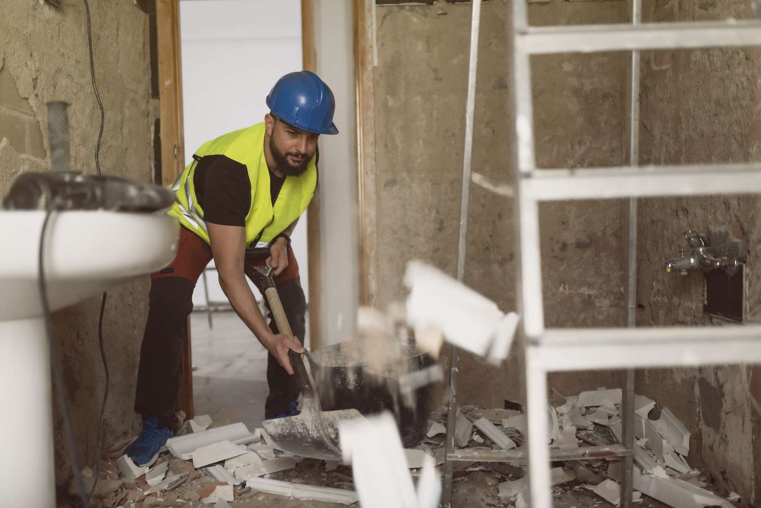 construction worker removes broken tiles with a shovel in a bathroom