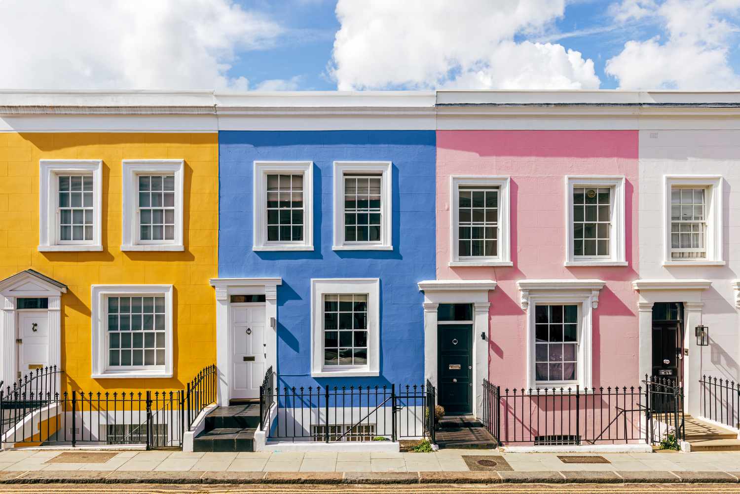 A sunny day on a street with colorful row houses that are backed by mortgages.