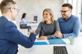 A younger couple looks happy as they shake hands with a financial professional.