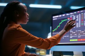 Woman sitting at a desk working on a large computer with charts and data.