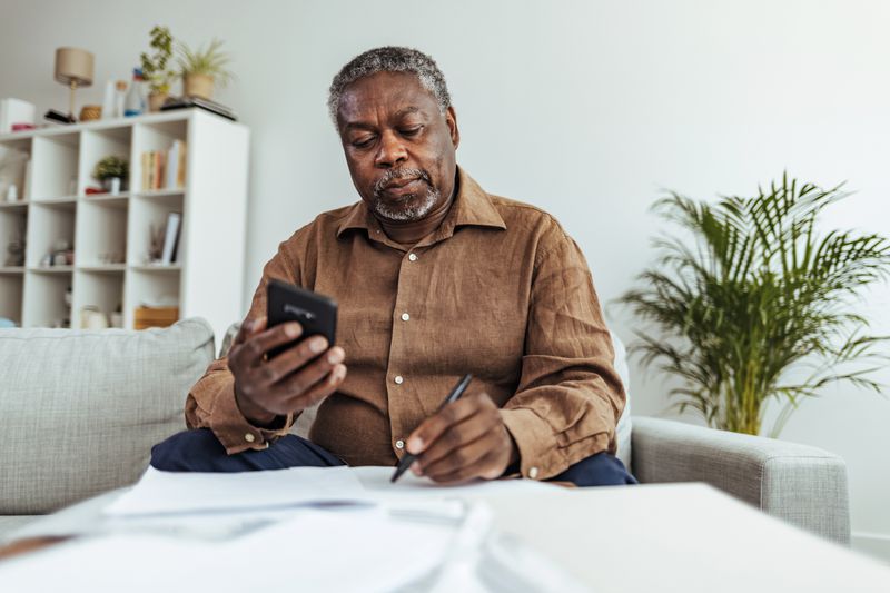 Senior Adult Man With Stacks of Papers and Envelopes holding a smartphone