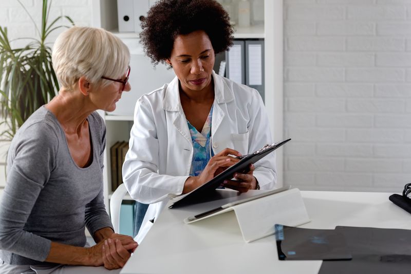 A female doctor sits at her desk and chats to an older female patient while looking at her test results