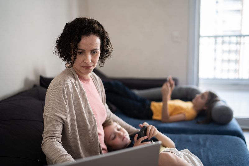Woman in her 40s sitting on her sofa, with her kids in nearby, looking at online bank rates