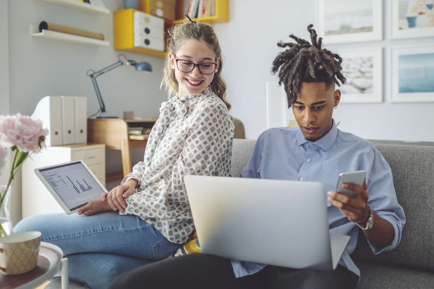 Two individuals research possible investments on their internet-connected devices while relaxing in a home office. 