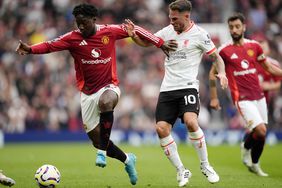 A Manchester United player dribbles a soccer ball away from a Liverpool player.