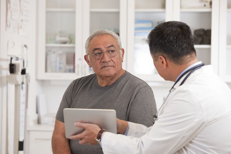 An older adult getting checked out by a doctor who is holding a tablet.