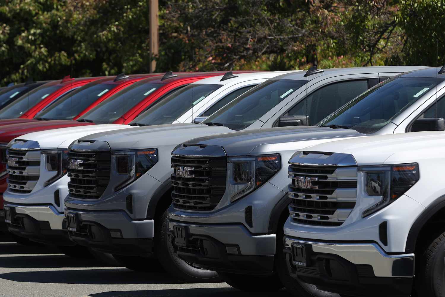 Several GMC trucks sit in a row in a dealership parking lot.