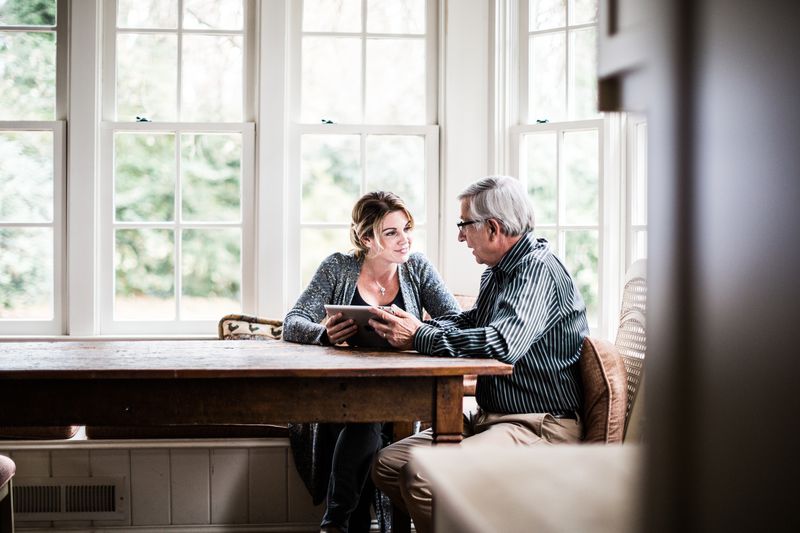 Father and daughter at a kitchen table looking at a tablet.