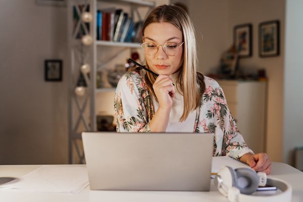 Young woman sitting at a desk at home and looking seriously at something on her laptop