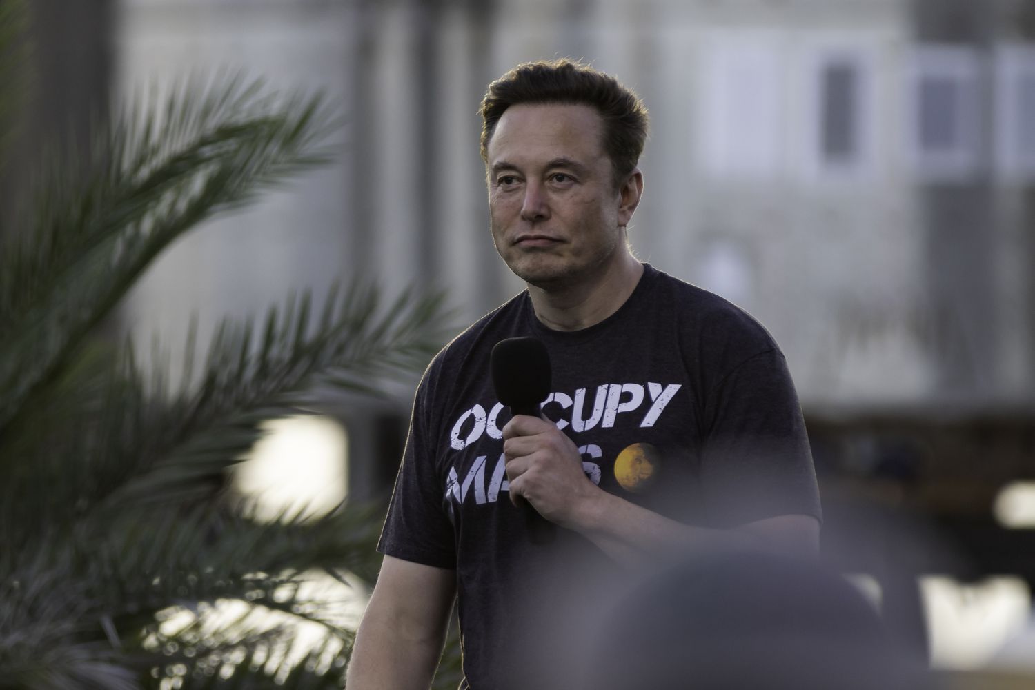 Elon Musk with a microphone wearing a t-shirt that says "Occupy Mars"