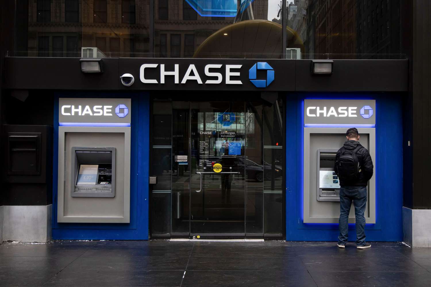 A man uses an ATM with the Chase logo visible above the two ATMs.