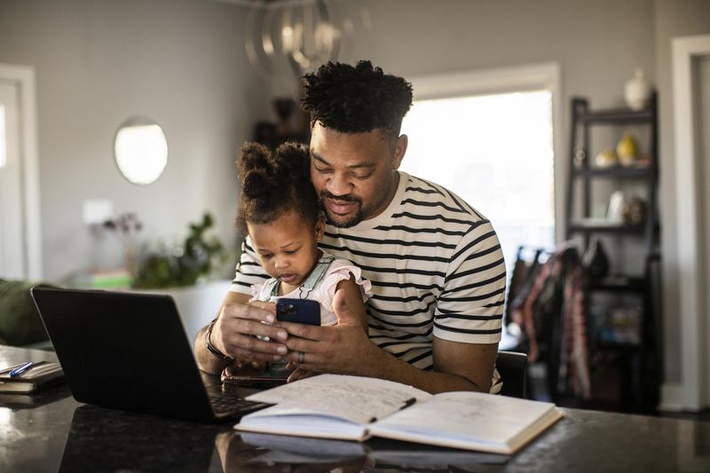 A man checks his investments on the computer with his child sitting in his lap