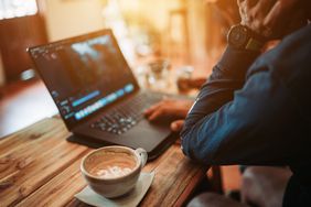 Person sitting at a table working on a laptop with a cup of coffee beside them.