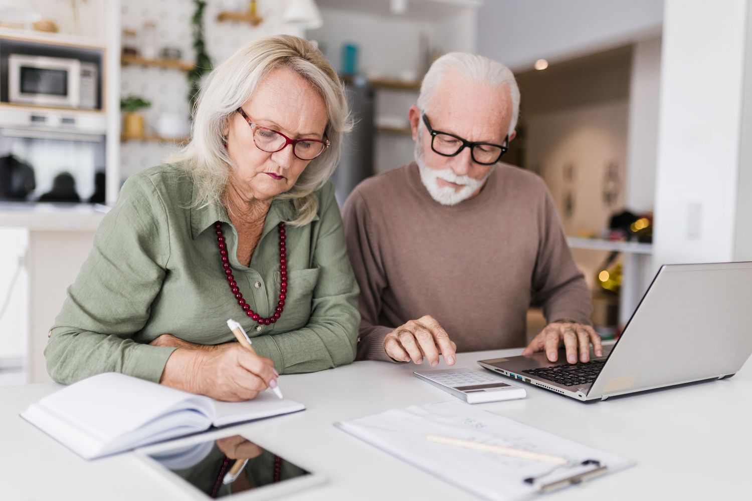 Two older adults focused on paperwork and a laptop on a table