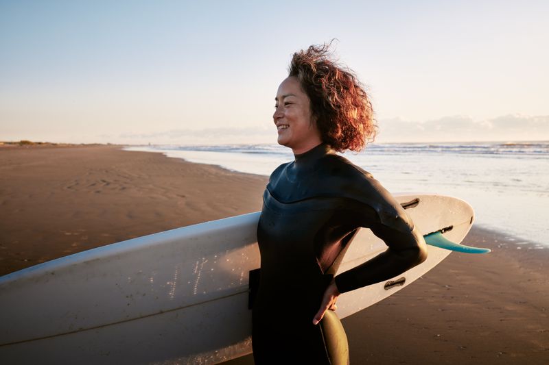 Woman on a beach with her surfboard, smiling. 
