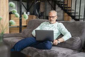 Man in in his 50s sitting on his sofa and looking intently at something on his laptop
